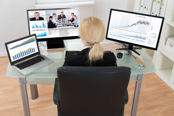 Blond businesswoman on a video conference call with laptop and two monitors on her desk