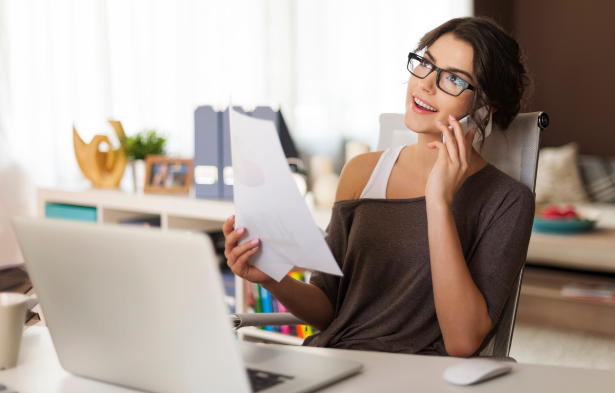 Woman on Cell Phone in Front of Laptop Working from Home Office