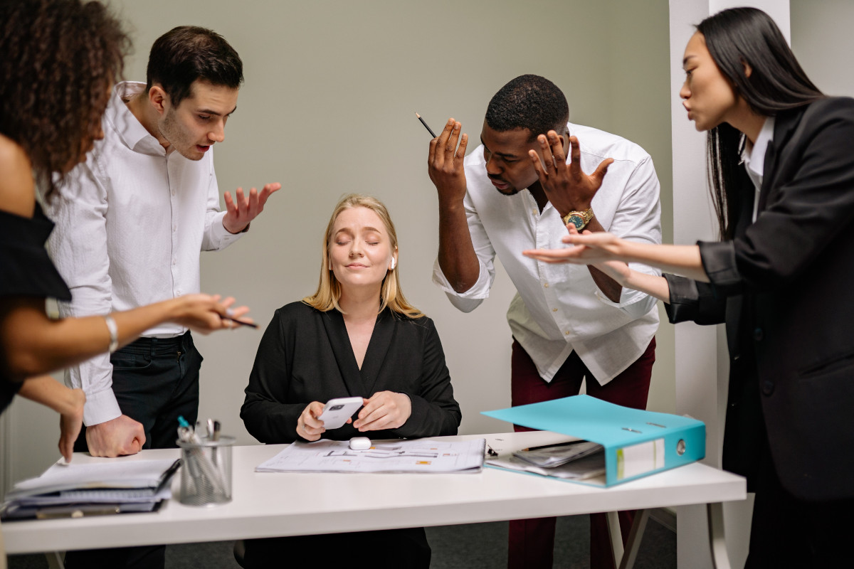 4 business people gesturing angrily at a blonde woman who has her eyes closed