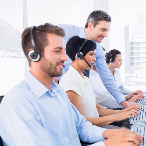 Call center workers wearing a headset, while a manger monitors their work closely